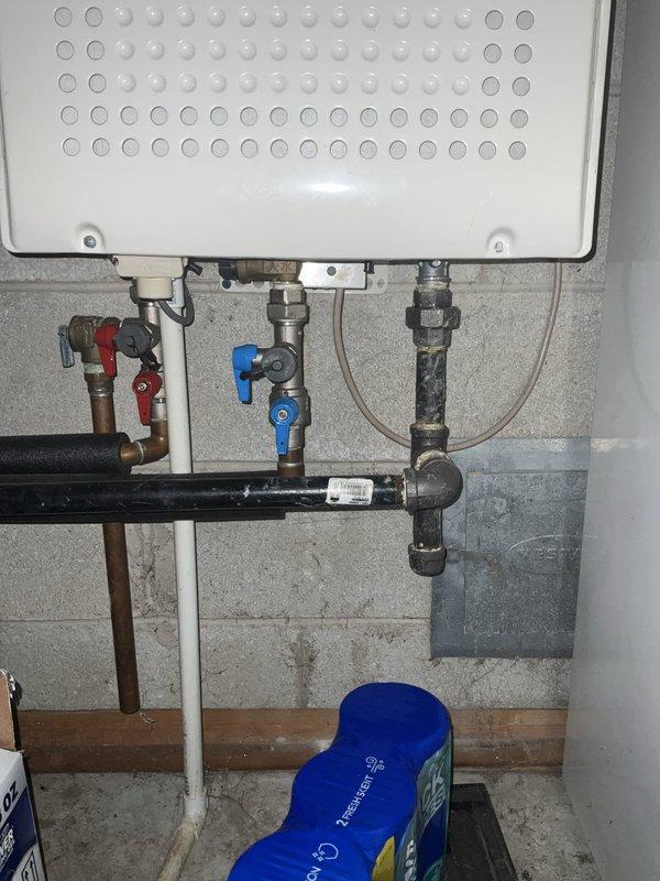 Conducted on-site assessment and provided estimate for replacement of existing 20+ year old water heater. Evaluated current installation including wall-mounted unit with copper and plastic supply lines, multiple shut-off valves (blue and red-handled ball valves), and connections to existing plumbing system. Documented basement utility area installation with concrete block wall mounting, mixed copper and plastic piping configuration showing signs of age and previous modifications. Photographed current setup including perforated bottom panel access, metal fittings, black horizontal pipe runs, and adjacent HVAC ductwork and PVC drainage systems. Provided comprehensive replacement options and recommendations based on existing infrastructure and client requirements.