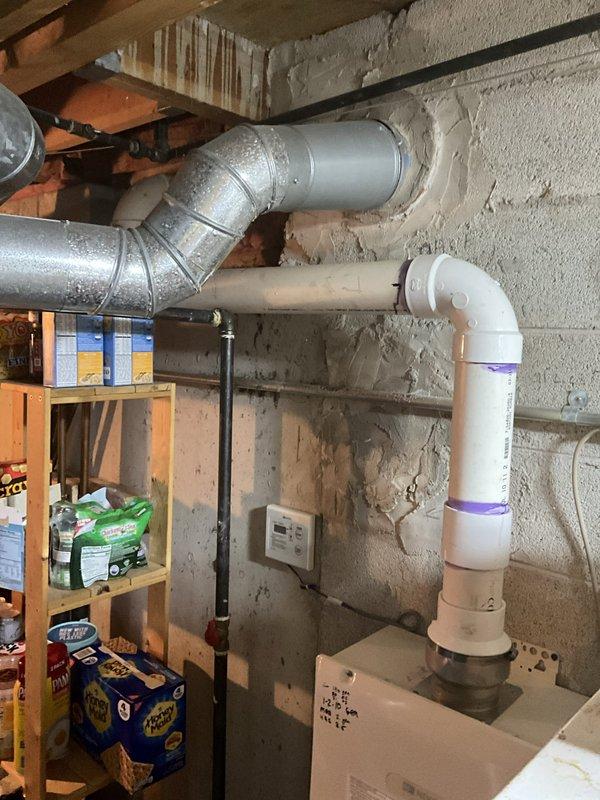 Conducted on-site assessment and provided estimate for replacement of existing 20+ year old water heater. Evaluated current installation including wall-mounted unit with copper and plastic supply lines, multiple shut-off valves (blue and red-handled ball valves), and connections to existing plumbing system. Documented basement utility area installation with concrete block wall mounting, mixed copper and plastic piping configuration showing signs of age and previous modifications. Photographed current setup including perforated bottom panel access, metal fittings, black horizontal pipe runs, and adjacent HVAC ductwork and PVC drainage systems. Provided comprehensive replacement options and recommendations based on existing infrastructure and client requirements.