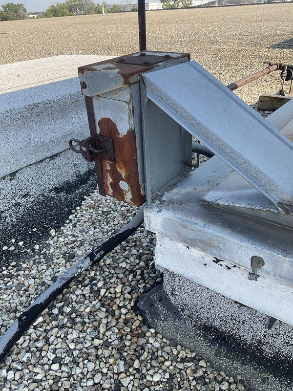 Conducted site assessment for commercial rooftop unit replacement project on flat gravel roof. Documented existing RTU installation including metal framework, ductwork assemblies, and associated piping systems showing extensive weathering and corrosion. Photographed rusted mounting brackets, oxidized pipe connections with teal-colored valve components, and deteriorated structural supports to determine replacement specifications. Evaluated rooftop access conditions and operational constraints for equipment installation during designated business hours from early morning through evening operations.
