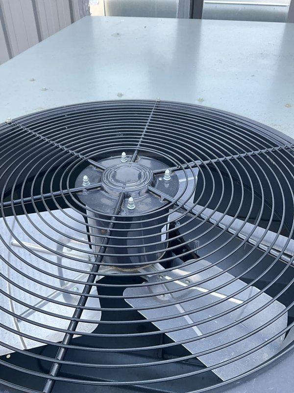 Responded to non-member service call for commercial ground-mounted package unit reported as non-operational since previous Wednesday. Upon arrival, inspected exterior-mounted HVAC unit with upward-discharge ductwork configuration. Performed diagnostic assessment of condenser fan assembly and motor hub, examining protective grille and blade operation. Evaluated electrical disconnect, refrigerant line connections, and overall unit condition. Documented equipment status with photos showing fan assembly components and complete unit installation on concrete pad. Unit operational status verified and customer advised of findings.