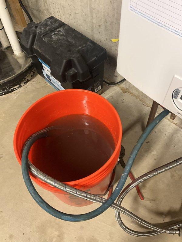 Performed comprehensive annual maintenance on wall-mounted tankless water heater unit. Flushed system using descaling solution to remove mineral buildup and sediment accumulation from heat exchanger, as evidenced by the reddish-brown discharge water collected during the cleaning process. Inspected all copper supply lines, PVC venting connections, and mounting hardware for proper installation and secure attachment to foundation wall. Verified unit operation and confirmed optimal performance upon completion of tune-up service.