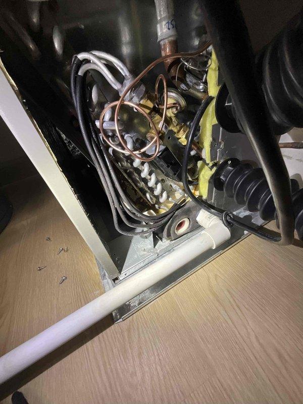 Responded to service call for water pooling under four-month-old furnace near AC drain line. Upon inspection, identified constant leak originating from condensate drainage system. Examined HVAC equipment including R-454B refrigerant system with A2L safety classification manufactured in April 2026. Inspected internal components including evaporator coil assembly with copper refrigerant lines, condensate pan, and drainage connections. Traced leak source to condensate drain line issue at PVC connection point. Documented equipment condition and drainage system configuration with photographs showing piping connections, coil assembly, and affected area. Cleared blockage and verified proper drainage flow through white PVC condensate line to eliminate standing water beneath unit.