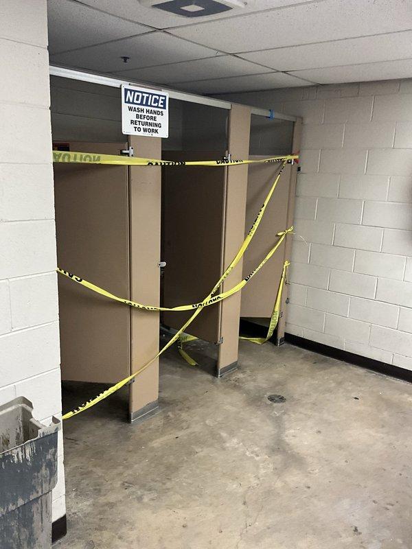 Responded to report of water intrusion through plumbing pipes in commercial restroom facility. Upon arrival, found evidence of water accumulation on concrete floor near urinal fixtures and floor drain, with visible staining and moisture patterns indicating recent or ongoing leak. Inspected three wall-mounted urinals with chrome flush valves and associated supply piping for source of water intrusion. Bathroom stalls cordoned off with caution tape due to facility conditions. Documented existing floor discoloration, water stains, and drain location for assessment. Investigation completed and photographic documentation obtained for further evaluation of plumbing system issues.