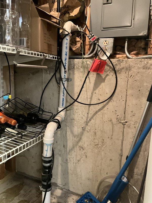 Performed complimentary sump pump inspection in basement utility area. Examined sump pump basin, discharge piping, and electrical connections for proper operation and potential issues. System components were found to be functioning, with white PVC discharge pipe properly secured and routed vertically through the space. Noted evidence of moisture and mineral deposits on concrete floor surrounding the basin, indicating normal historical pump operation. All electrical connections and wiring appeared secure at the junction box. No immediate repairs or adjustments were required at time of inspection.