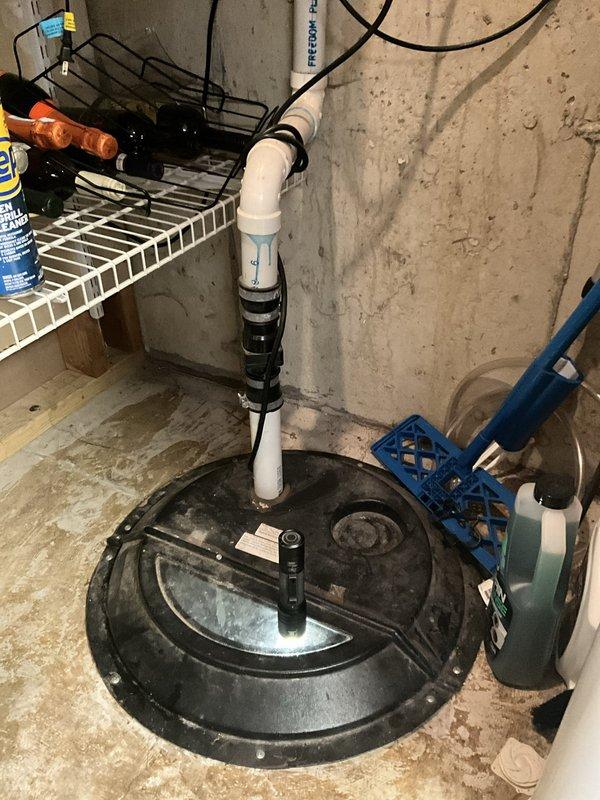 Performed complimentary sump pump inspection in basement utility area. Examined sump pump basin, discharge piping, and electrical connections for proper operation and potential issues. System components were found to be functioning, with white PVC discharge pipe properly secured and routed vertically through the space. Noted evidence of moisture and mineral deposits on concrete floor surrounding the basin, indicating normal historical pump operation. All electrical connections and wiring appeared secure at the junction box. No immediate repairs or adjustments were required at time of inspection.
