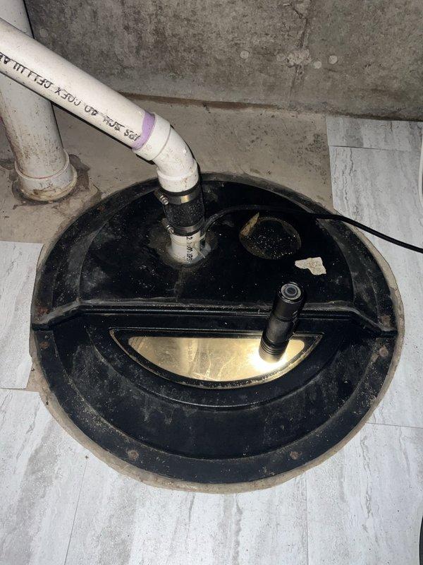 Performed complimentary sump pump inspection. Verified proper operation of sump pump system, including pit assembly with black circular cover, PVC discharge piping with rubber coupling and metal clamp connections, and secondary drainage line. Inspected vertical discharge pipe routing along foundation wall with elbow joint connection. All components found to be functioning properly with adequate water level in pit and secure pipe connections. System operational and ready for continued service.