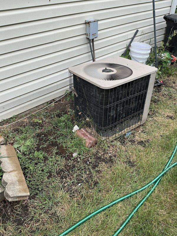 Completed HVAC estimate for full system replacement on residential property with 17+ year old equipment. Client's existing furnace has a damaged heat exchanger requiring immediate replacement for safety concerns. Evaluated outdoor condensing unit positioned against house exterior, noting significant age-related deterioration, weathering, and accumulation of dirt and debris on surfaces. Unit shows clear signs of extended service life with worn components and requires replacement along with indoor coil to ensure proper system matching and efficiency. Documented existing electrical disconnect box and conduit configuration for replacement planning. Provided comprehensive estimate for new furnace and air conditioning system installation to address failed heat exchanger and aging equipment concerns.