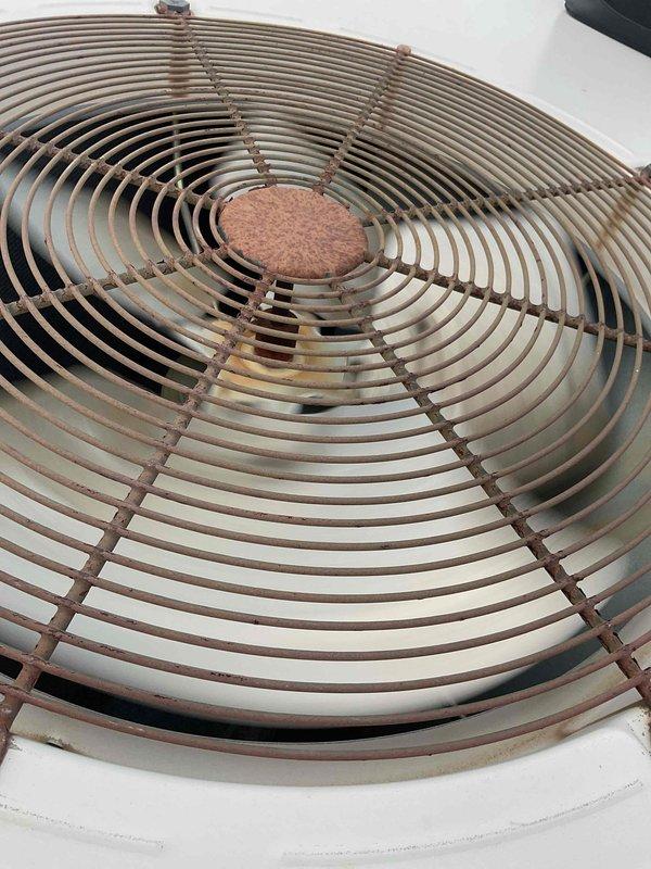 Responded to commercial no cooling call for rooftop unit. Upon arrival, accessed RTU via ladder and performed diagnostic inspection. Found condenser fan motor inoperative with visible signs of weathering, corrosion, and age-related deterioration on fan guard and motor assembly. Thermostat was powered but unable to initiate cooling mode due to failed outdoor unit operation. Inspected refrigerant piping connections, electrical components, and condensing unit assembly. Documented equipment condition with photos showing significant oxidation on fan motor hub and protective wire guard, indicating prolonged exposure to outdoor elements and end-of-service-life condition requiring replacement.