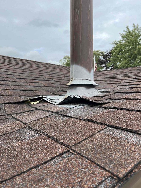 Responded to report of water leaking from residential HVAC unit. Upon inspection, identified the source as roof penetration failure at the flue pipe rather than the HVAC system itself. The rubber boot flashing surrounding the metal vent stack showed severe deterioration with torn sections peeling away from the pipe, creating gaps that allowed water infiltration. The storm collar and flashing materials at the pipe base were compromised, with visible separation and curling of the weatherproofing components. Multiple asphalt shingles surrounding the penetration point exhibited cracking, lifting, and damage, with exposed underlayment visible in several areas. Documented extensive deterioration including granule loss on shingles, debris accumulation, and weathering stains on the pipe surface. Advised that the water leak was originating from failed roof flashing and penetration sealing at the flue pipe, not from the HVAC equipment. Recommended immediate roof repair by qualified roofing contr