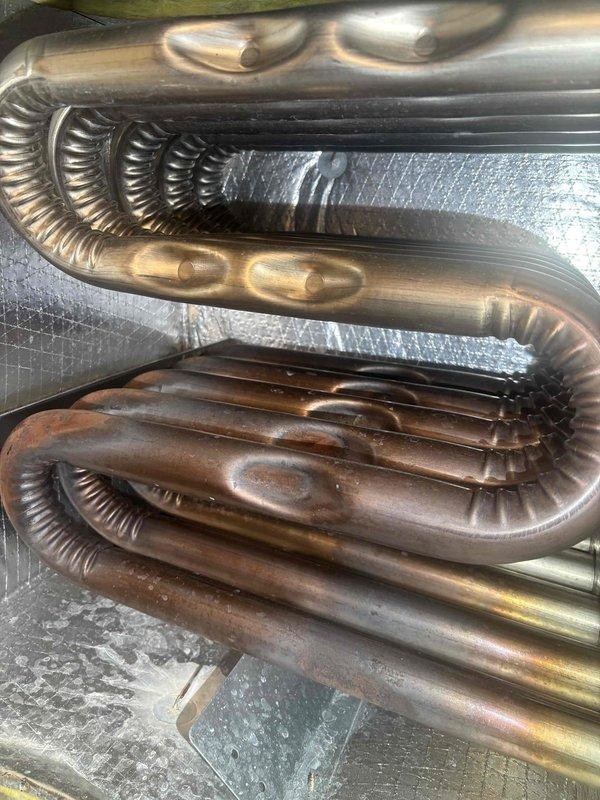 Completed comprehensive BFMA tune-up service including furnace inspection, air conditioning system maintenance, and dryer vent cleaning. Inspected heat exchanger coils and noted progressive corrosion on lower copper tubing sections with oxidation present, while upper coils remain in good condition. Examined and tested flame sensor for proper operation, verified all safety controls, cleaned components as needed, and documented system condition with photographic evidence for maintenance records.