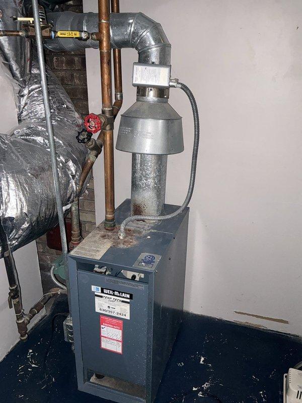 Completed installation of a combi boiler system in mechanical utility room, including all necessary connections for heating and domestic hot water supply. Installed copper piping with isolation valves, metallic ductwork with curved elbow connection for exhaust venting, and flexible metal conduit for electrical connections. Additionally installed a Richmond brand water heater in adjacent utility closet with proper venting and plumbing connections to ensure full system functionality.