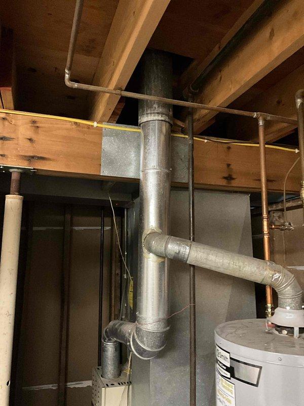 Completed comprehensive tune-up service on 30-year-old HVAC system including both furnace and air conditioning units located in basement utility area. Performed full inspection of vertical furnace unit, ductwork system including galvanized metal runs with multiple bends and connections, and associated components. Evaluated aging equipment condition, verified proper operation of heating and cooling systems, and documented equipment status with photographic records of furnace, ductwork configuration, and mechanical room layout for maintenance records.