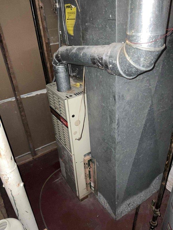Completed comprehensive tune-up service on 30-year-old HVAC system including both furnace and air conditioning units located in basement utility area. Performed full inspection of vertical furnace unit, ductwork system including galvanized metal runs with multiple bends and connections, and associated components. Evaluated aging equipment condition, verified proper operation of heating and cooling systems, and documented equipment status with photographic records of furnace, ductwork configuration, and mechanical room layout for maintenance records.