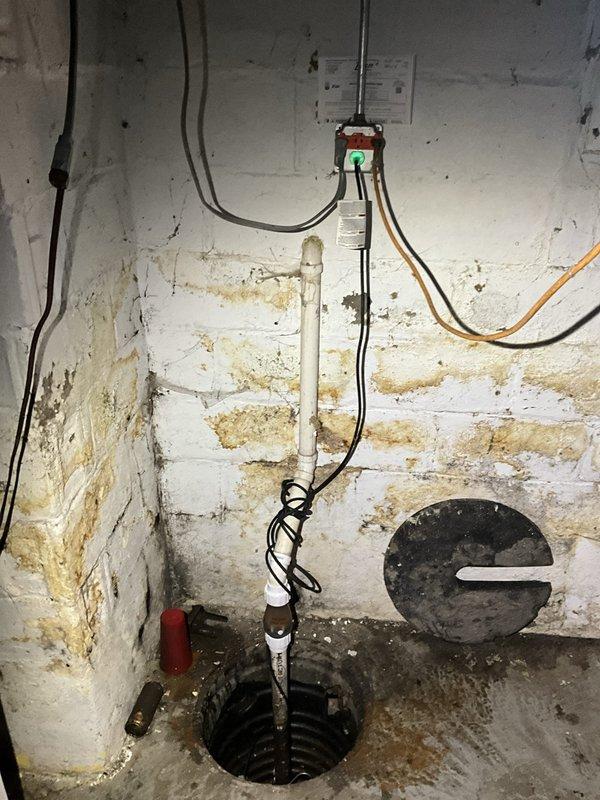 Responded to sump pump failure caused by burned-out motor unit. Upon arrival, assessed existing sump pump installation in basement environment showing significant historical water infiltration and moisture damage to surrounding concrete block walls. Removed failed pump from circular sump pit and verified electrical connections and discharge piping configuration. Installed replacement sump pump unit, reconnected white PVC discharge pipe with proper check valve assembly, and secured all electrical wiring according to code requirements. Tested pump operation including float switch functionality to ensure proper activation and water evacuation. Verified discharge flow through existing piping system and confirmed system cycling correctly under simulated conditions.