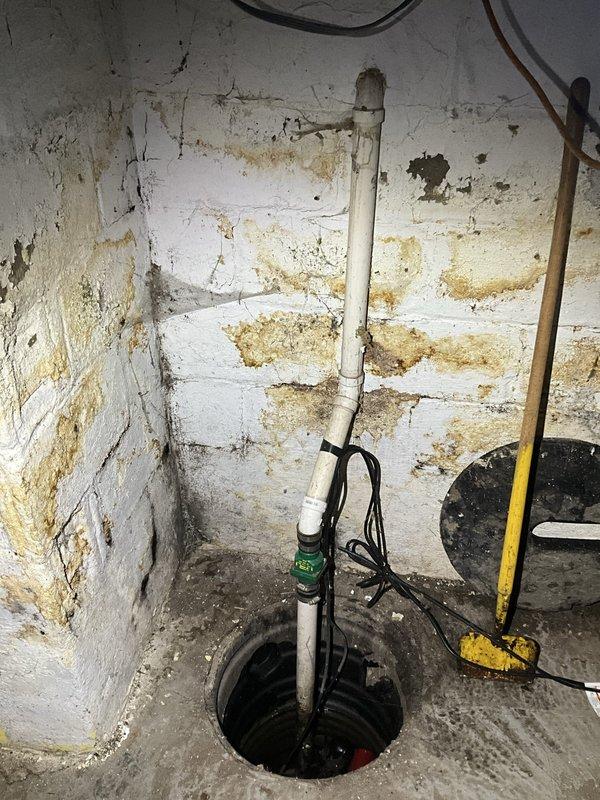 Responded to sump pump failure caused by burned-out motor unit. Upon arrival, assessed existing sump pump installation in basement environment showing significant historical water infiltration and moisture damage to surrounding concrete block walls. Removed failed pump from circular sump pit and verified electrical connections and discharge piping configuration. Installed replacement sump pump unit, reconnected white PVC discharge pipe with proper check valve assembly, and secured all electrical wiring according to code requirements. Tested pump operation including float switch functionality to ensure proper activation and water evacuation. Verified discharge flow through existing piping system and confirmed system cycling correctly under simulated conditions.