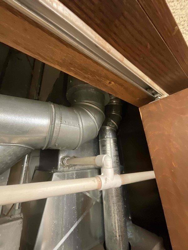 Conducted site assessment for commercial air conditioning and coil replacement estimate. Customer requested second opinion after another contractor recommended complete HVAC system replacement including furnaces. Inspected existing dual Carrier furnace installation located in utility room with side-by-side configuration. Evaluated ductwork system including horizontal metal supply ducts, flexible ductwork connections, and PVC condensate drain lines. Assessed confined space mechanical area beneath structural elements containing integrated HVAC and plumbing systems. Photographed existing equipment including furnace units with specification labels, galvanized metal plenum, gray ductwork, and water heater. Documented current system configuration to determine scope of work required for air conditioning and coil replacement without unnecessary furnace removal. Provided comprehensive evaluation to offer alternative solution focused specifically on AC and evaporator coil replacement needs.