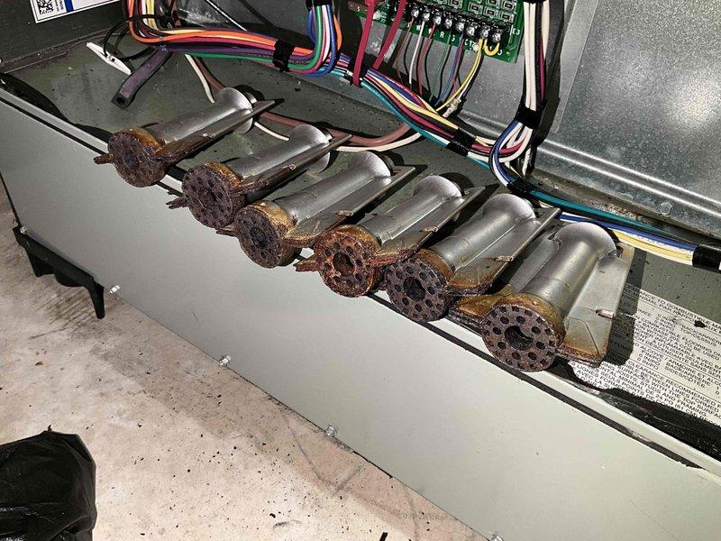 # Furnace Winter Tune-Up Completed

Performed comprehensive winter tune-up on 4-year-old Trane furnace system located in basement. Conducted full system diagnostics including electrical testing with digital multimeter to verify proper voltage and amperage across all circuits. Inspected control board wiring, relay functions, and electrical connections throughout the system.

During inspection, identified moderate to heavy rust and corrosion on burner assembly components, specifically on the burner ports and flame sensor area. Corrosion appears consistent with normal condensation exposure over the unit's operational period but will require monitoring for potential performance impact. All burner orifices show surface oxidation with visible rust discoloration on perforated surfaces.

Tested all safety controls, limit switches, and flame sensors for proper operation. Verified ignition sequence, flame characteristics, and burner operation across all zones. Confirmed proper airflow through he