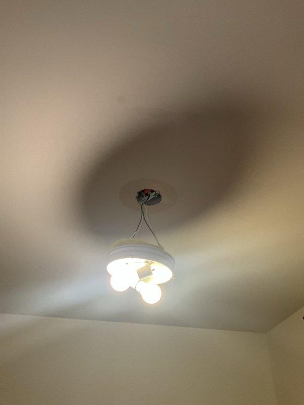 Responded to a reported bathtub leak and inspected the fixture, finding the handle removed and the escutcheon, valve cartridge housing, and splined stem exposed with visible wear at the housing rim. Accessed the valve assembly to diagnose the leak source, and the ceiling light fixture below was found disconnected from its mounting plate and hanging by its wires from the junction box, likely due to water intrusion or access work.