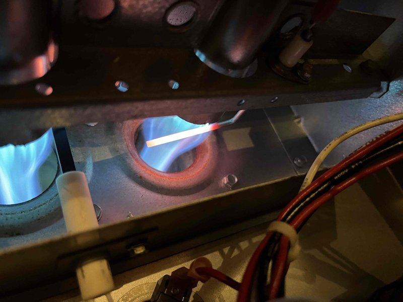 Sold repair for flame sensor replacement. Removed heavily degraded flame sensor from heating system showing compromised combustion operation, as evidenced by visible flame pattern through inspection port. Installed new flame sensor, restoring proper flame detection capability to ensure reliable system operation.