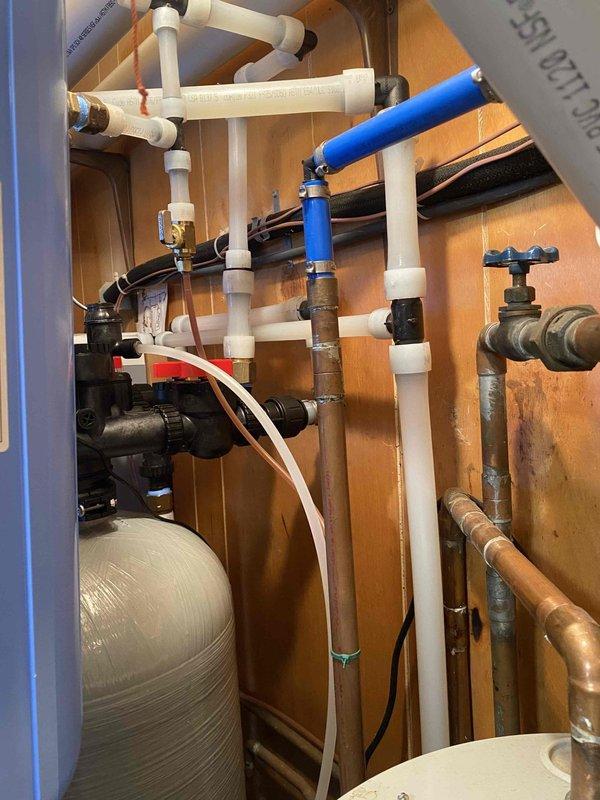 Removed existing water conditioning system and installed new Water Right IMPBF-1054AN acid neutralizer with calcite to address acidic water issues, along with Water Right ASP1-1354 sanitizer with min-plus for iron, hardness and odor treatment. Completed necessary repiping of water lines in closet using PEX material, ensuring proper connection to both treatment units mounted on wooden wall.