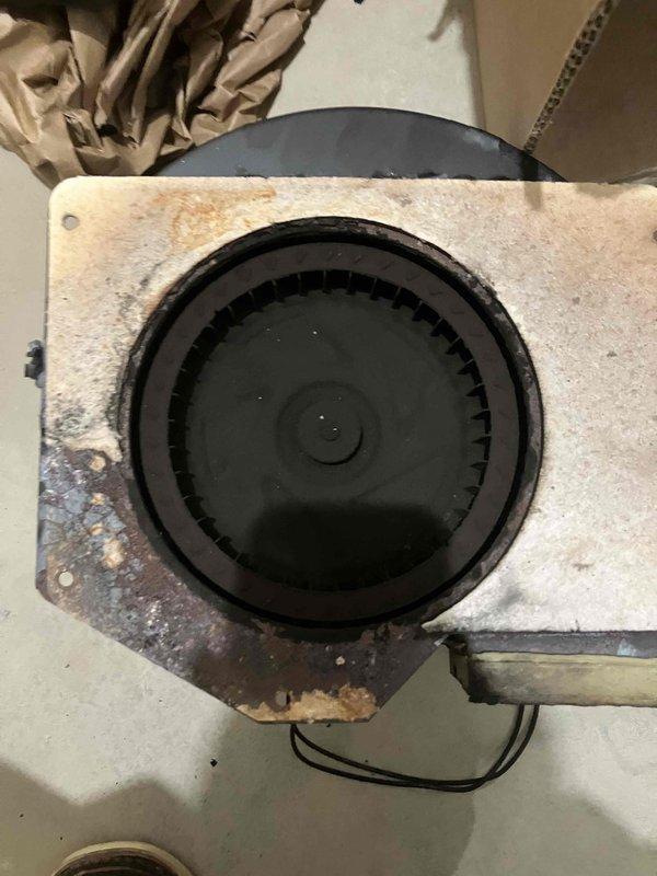 Replaced severely deteriorated inducer motor assembly that was causing system overheating. Visual inspection revealed significant corrosion, rust damage, and soot buildup throughout the assembly. Inducer fan wheel showed extensive wear with damaged blades and mounting plate exhibited heavy discoloration and rust penetration around the vent opening.