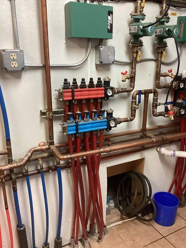 Performed emergency service on residential hydronic heating system with leaking manifold. Inspected the system which included copper piping, Taco control box, green circulator pumps, and PEX tubing zones. Replaced the faulty manifold to resolve the leak, ensuring proper pressure and operation of the in-floor heating system.