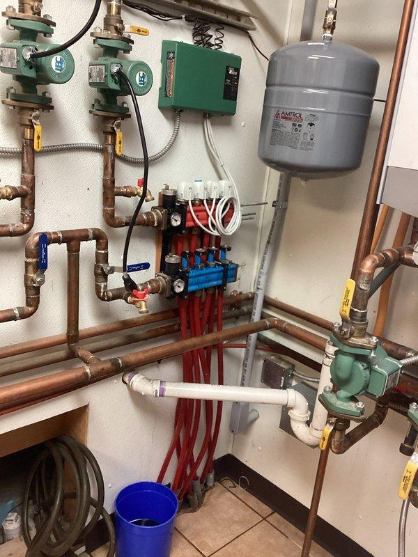 Performed emergency service on residential hydronic heating system with leaking manifold. Inspected the system which included copper piping, Taco control box, green circulator pumps, and PEX tubing zones. Replaced the faulty manifold to resolve the leak, ensuring proper pressure and operation of the in-floor heating system.