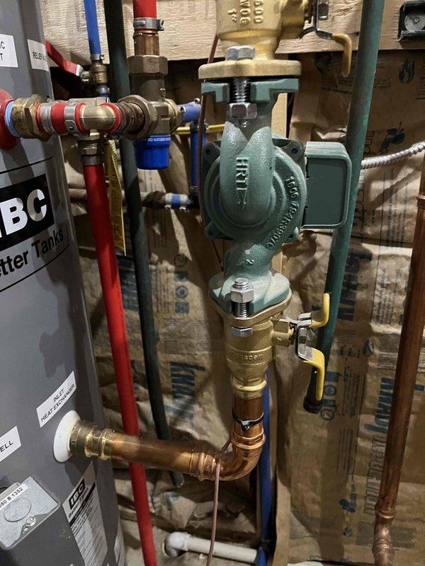 Responded to report of leaking black substance from accessory tank connected to IBC boiler system. Upon inspection, identified multiple leak sources including expansion tank with corrosion penetration above diaphragm releasing antifreeze sludge, aged indirect water heater with internal leak, and corroded connections at infloor heating manifold. Performed immediate repair on expansion tank to stop active leakage. System includes teal circulator pump, brass and copper piping with PEX connections, pressure gauge, and multi-zone manifold distribution assembly for radiant floor heating. Customer advised of additional repairs needed for water heater replacement and manifold connection rehabilitation, estimates to follow.