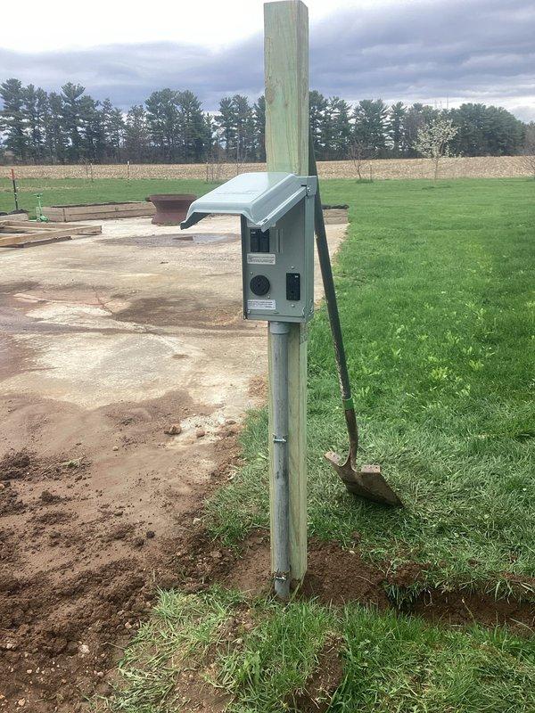 Removed existing 50A welder receptacle from building exterior and installed junction box to extend the circuit. Mounted 30/20 RV service panel on treated wooden post in yard area, running conduit from the building-mounted junction box down through the corrugated metal siding to ground level and across to the post-mounted panel. Connected the extended circuit to the RV panel and installed the required breaker to complete the electrical service, as the circuit was previously disconnected.