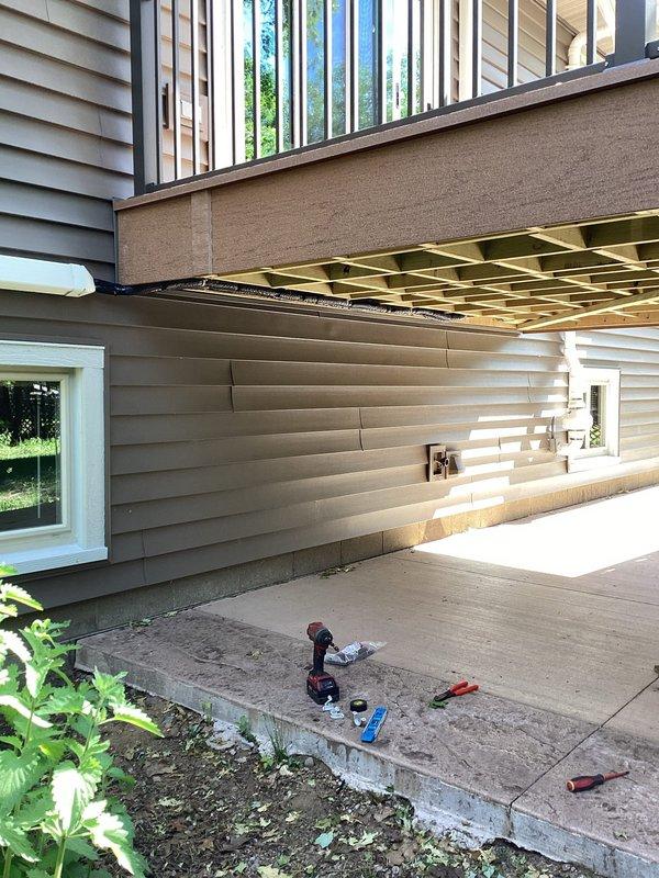 Leveled outdoor condenser unit using gravel placed underneath the support platform to ensure proper positioning. Installed 12 feet of lineset covers under the deck structure with three 90-degree elbows to protect refrigerant lines and provide a professional finished appearance.