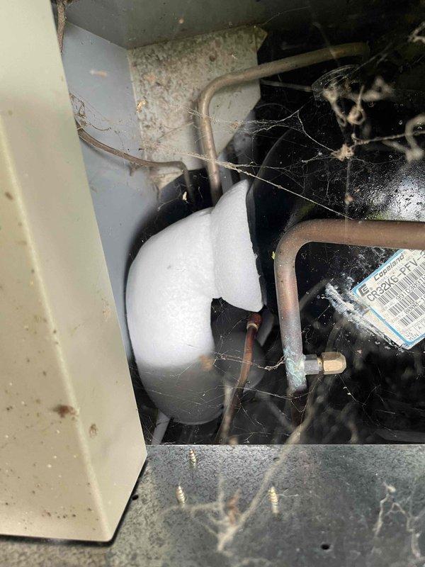 Upon arrival, found the air conditioning system running but unable to maintain temperature below 78 degrees. Inspection revealed extensive ice buildup from the evaporator coil through the refrigerant lines extending all the way to the compressor and accumulator. The outdoor unit showed signs of age with weathering and debris accumulation around the base. The indoor compartment displayed significant dust, cobwebs, and lack of recent maintenance. Documented the iced refrigerant system and overall condition of the aging equipment with photos. Provided estimates for necessary repairs to restore proper cooling operation.