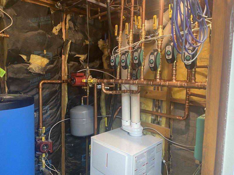 Completed return visit to finish zone valve manifold piping installation on hydronic heating system. Replaced corroded fittings in ceiling using press fittings (four 1" UFS-100P and two 3/4" UFS-075P for Taco zone valves), installed six 1¼" x 1¼" x ¾" tees and two 1¼" x 1¼" x 1" tees to complete manifold assembly. Charged system with Alpha 11 antifreeze and purged all air from heating loops. Resolved leaking fittings, tested all zones for proper operation, and restored system to full heating functionality including both domestic hot water loop and all heating zones.