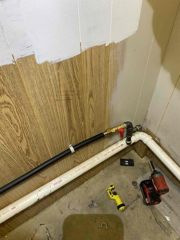 Installed new gas piping system for dual dryer setup in laundry room. Tied into existing gas line above boiler at unused fitting, installing 1/2" black iron tee with two shutoffs—one remaining plugged for future use and one adapted to TracPipe. Ran TracPipe gas line into laundry room behind existing dryer location, installed trac tee fitting above first dryer, and extended additional gas line along ceiling to second future dryer location. All connections secured with appropriate shutoff valves and fittings per code requirements.