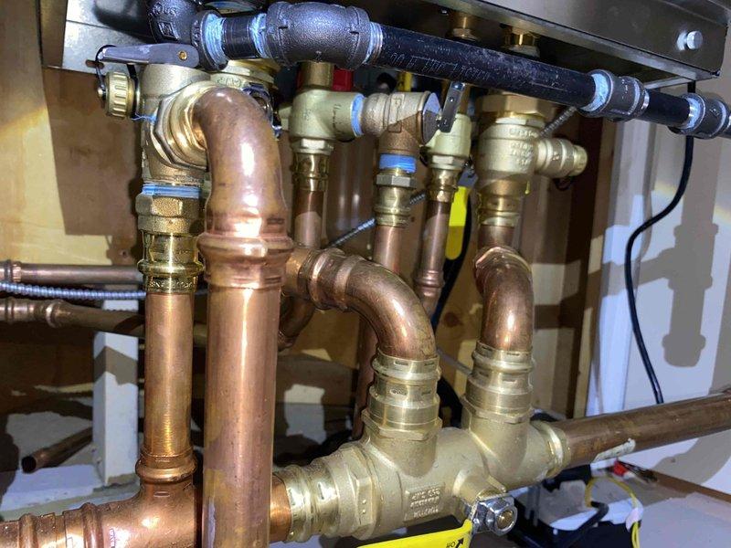 Installed new gas piping system for dual dryer setup in laundry room. Tied into existing gas line above boiler at unused fitting, installing 1/2" black iron tee with two shutoffs—one remaining plugged for future use and one adapted to TracPipe. Ran TracPipe gas line into laundry room behind existing dryer location, installed trac tee fitting above first dryer, and extended additional gas line along ceiling to second future dryer location. All connections secured with appropriate shutoff valves and fittings per code requirements.