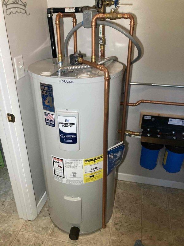 Installed Bradford White tanked water heater with complete plumbing connections including copper piping, pressure relief valve, and associated fittings. Additionally installed water filtration system with blue cylindrical filter canisters, pressure tank, and round toilet with 17-inch height specification to complete the plumbing upgrade.