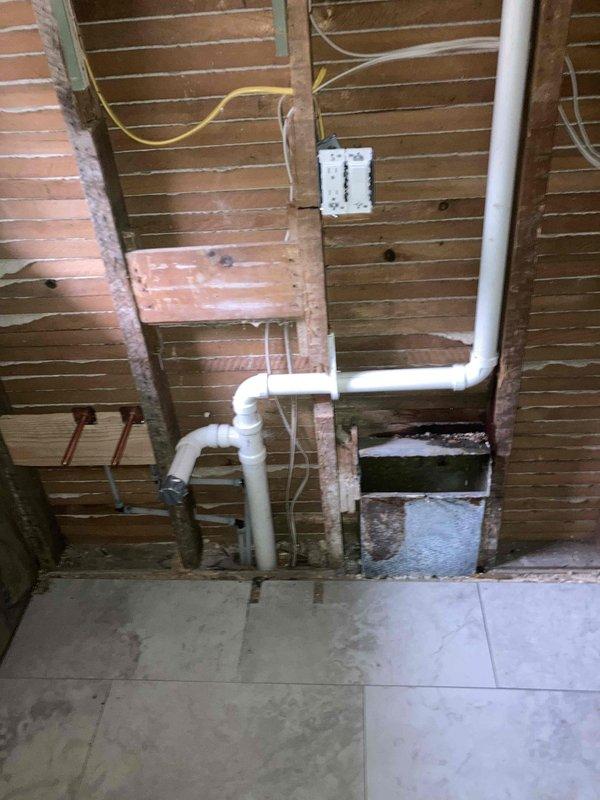 Removed existing cast iron toilet flange, galvanized lavatory drain, 3" cast iron vent pipe up to bathroom closet midpoint, and main cleanout. Tied into existing 3" cast vent in bathroom closet from 5' elevation down to floor level, connecting galvanized vent pipe for lavatory and new shower trap. Ran new PVC drainage piping approximately 3' into crawlspace and installed new main cleanout. Set new toilet flange and stubbed out new PVC for lavatory drain. Installed new toilet, connected tub/shower waste and overflow assembly, and set lavatory faucet. Positioned vanity and completed plumbing connections.