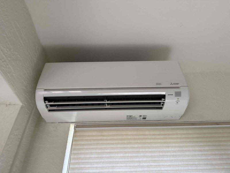 Performed scheduled preventative maintenance on wall-mounted Mitsubishi ductless mini-split air conditioning unit as part of quarterly service agreement (maintenance visit 3 of 4). Conducted comprehensive inspection of indoor evaporator unit, verifying proper mounting, checking louver operation and airflow direction, and examining unit housing for any signs of damage or deterioration. Cleaned air filters and exterior casing, tested control functions and indicator lights, and confirmed unit operational status. Documented equipment condition through photographic records showing unit installation, placement relative to ceiling and window, and overall system integrity. All components found in satisfactory working condition with no visible defects, proper louver alignment, and clean appearance indicating good system maintenance.