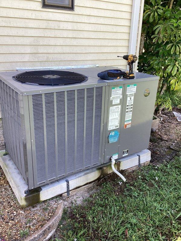 Responded to no cooling call with blank thermostat display on residential HVAC system. Upon arrival, found outdoor unit positioned on concrete pad with expired membership status. Performed diagnostic inspection of packaged air conditioning system, examining condenser unit, electrical connections, and thermostat communication. Documented equipment condition with photographs showing unit placement, manufacturer specifications, and surrounding installation area including condensate drain line and mounting configuration.
