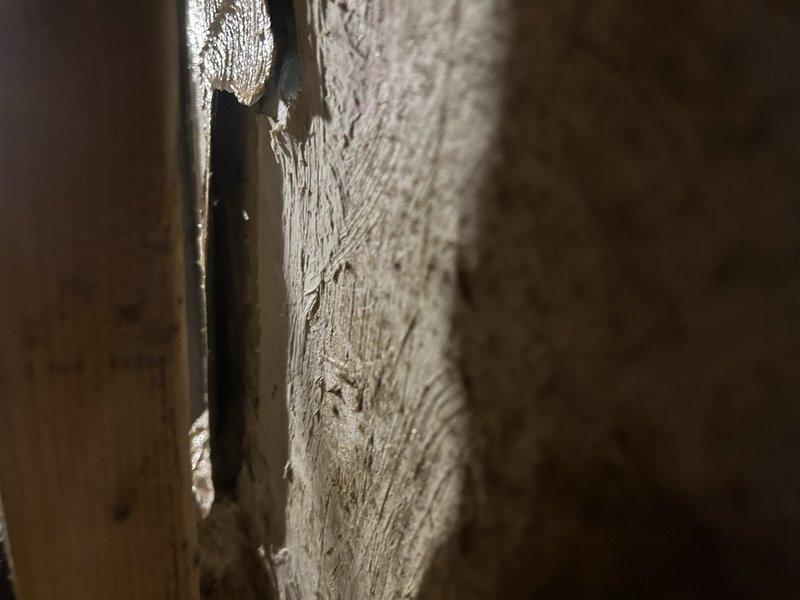 Sanibel, FL - Responded to report of water leaking in attic near ductwork. Upon inspection, discovered deteriorated wooden structural beam showing significant weathering, cracking, and fiber separation near HVAC components. Examined HVAC condensate management system including black metal drain pan positioned over floor joists with white PVC drainage line. Observed heavily oxidized copper refrigerant lines with discoloration and patina buildup wrapped with white insulation tape. Identified water staining and residue on drain pan surface indicating active condensate collection. Documented condition of wooden joists and structural elements in immediate vicinity of HVAC equipment. Photographed deteriorated wood framing, gap between structural components, and overall installation setup to determine source of water intrusion and assess extent of moisture damage to building materials.