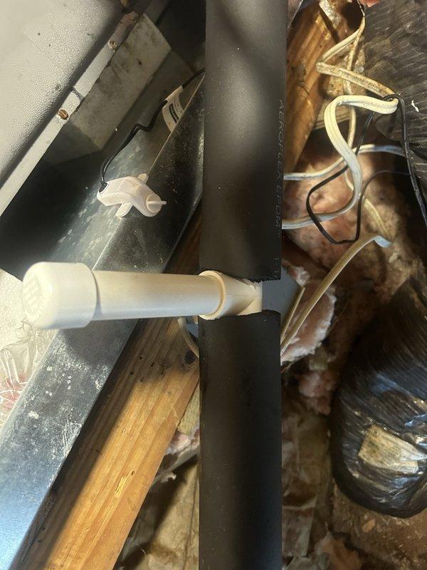 Sanibel, FL - Responded to report of water leaking in attic near ductwork. Upon inspection, discovered deteriorated wooden structural beam showing significant weathering, cracking, and fiber separation near HVAC components. Examined HVAC condensate management system including black metal drain pan positioned over floor joists with white PVC drainage line. Observed heavily oxidized copper refrigerant lines with discoloration and patina buildup wrapped with white insulation tape. Identified water staining and residue on drain pan surface indicating active condensate collection. Documented condition of wooden joists and structural elements in immediate vicinity of HVAC equipment. Photographed deteriorated wood framing, gap between structural components, and overall installation setup to determine source of water intrusion and assess extent of moisture damage to building materials.