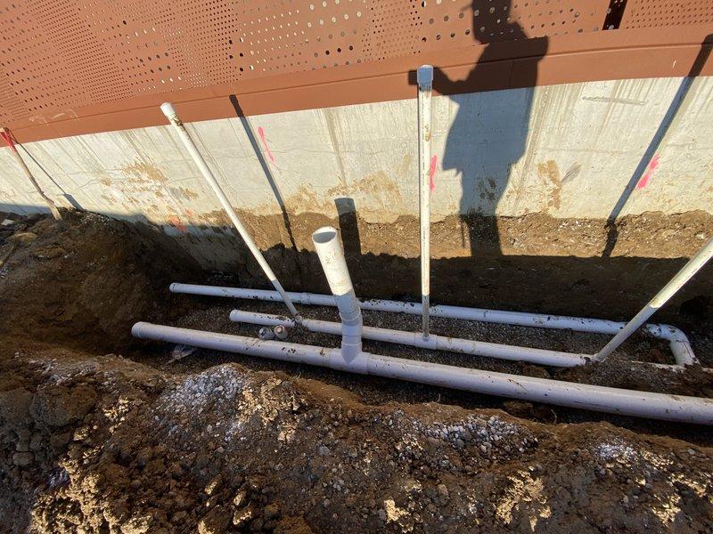 Completed installation of a new 4" discharge line into manhole with water stop per estimate. Work included excavating trench adjacent to foundation, laying and securing PVC piping according to permit specifications (24DRN-00132), and ensuring proper connection to existing drainage system. Photos documented the completed installation showing horizontal and vertical pipe placement with appropriate markers for elevation levels.