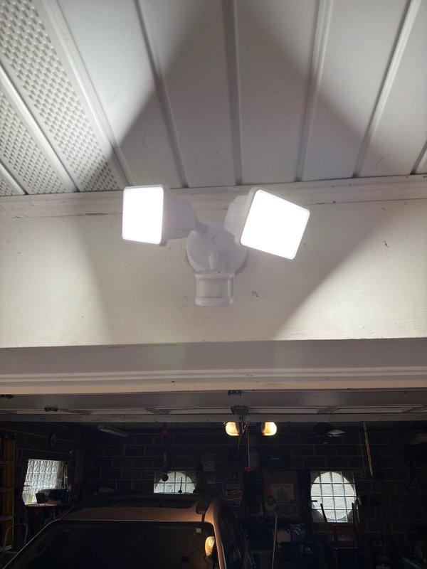 Installed dual-head motion sensor security light on exterior soffit above garage entrance. Mounted fixture securely to white ceiling surface and verified proper operation of both light panels and motion detection functionality.