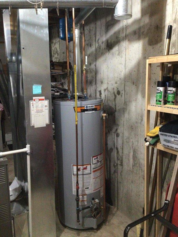 Successfully installed a 50-gallon tall gas water heater in basement utility room. Installed a blue expansion tank with proper mounting bracket to meet code requirements. All connections were completed with copper piping and included installation of the yellow gas line.