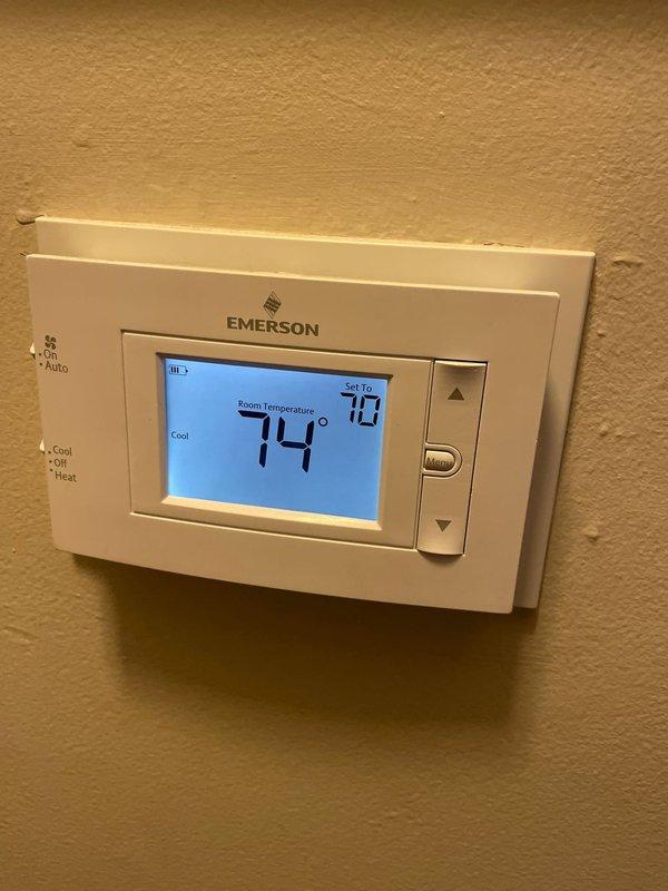 Performed diagnostic assessment on 9-year-old AC system installed in 2022, addressing customer complaint of reduced airflow despite cool air output. Inspected Emerson digital thermostat (functioning properly at 74°F with 70°F setpoint) and examined air handler unit with connected ductwork in utility area. Determined airflow restriction was caused by partially blocked evaporator coil; cleaned coil and verified improved system performance with proper airflow restored.