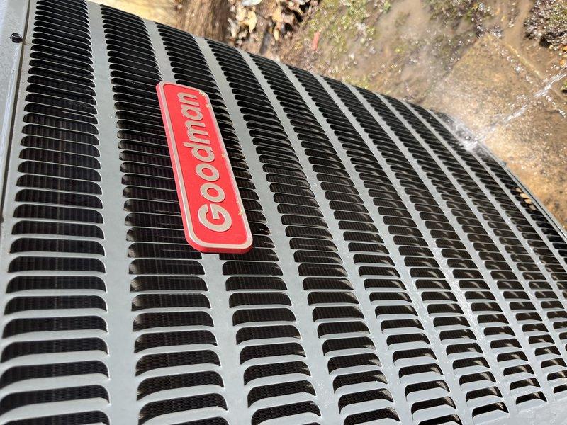 Performed scheduled tune-up maintenance on a Goodman AC unit (HD#F57544287). Inspected exterior condenser which is ground-mounted on concrete pad, showing signs of moisture pooling around base. Unit appears in functional condition with no visible damage, though surrounding area exhibits minor algae growth and weathering that may require attention in future service.