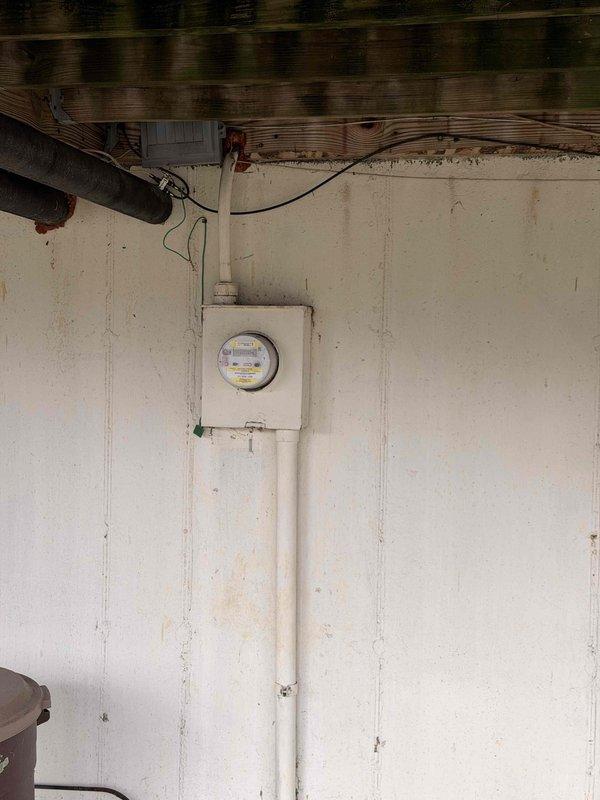 Completed annual electrical inspection, examining the main breaker panel which showed proper circuit organization but evidence of possible water damage on surrounding wall. Inspected exterior electrical meter installation with PVC conduit, noting normal operational status but minor weathering on the housing and mounting surface.