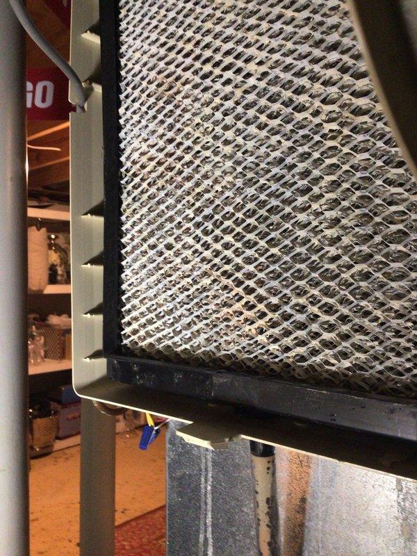 Responded to service call for leaking humidifier in HVAC system under 10 years old. Inspection revealed severely clogged air filter with significant dust accumulation and reddish-brown staining throughout the diamond-patterned mesh. Filter was replaced to restore proper airflow and address moisture issues causing the humidifier leak.