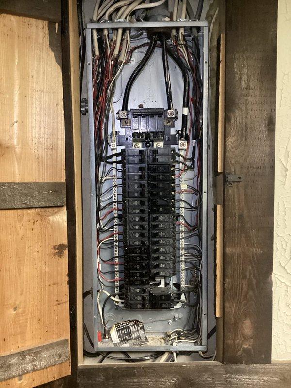Conducted a complimentary electrical inspection of the residential breaker panel, noting congested wiring with multiple colored conductors (black, white, red) and approximately 20 circuit breakers arranged in dual columns. Also examined an Eveready control panel mounted on framed wall structure with indicator lights and adjacent copper piping, documenting both systems with photographs for assessment purposes.