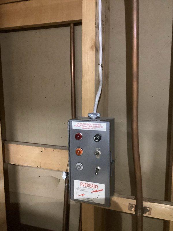 Conducted a complimentary electrical inspection of the residential breaker panel, noting congested wiring with multiple colored conductors (black, white, red) and approximately 20 circuit breakers arranged in dual columns. Also examined an Eveready control panel mounted on framed wall structure with indicator lights and adjacent copper piping, documenting both systems with photographs for assessment purposes.