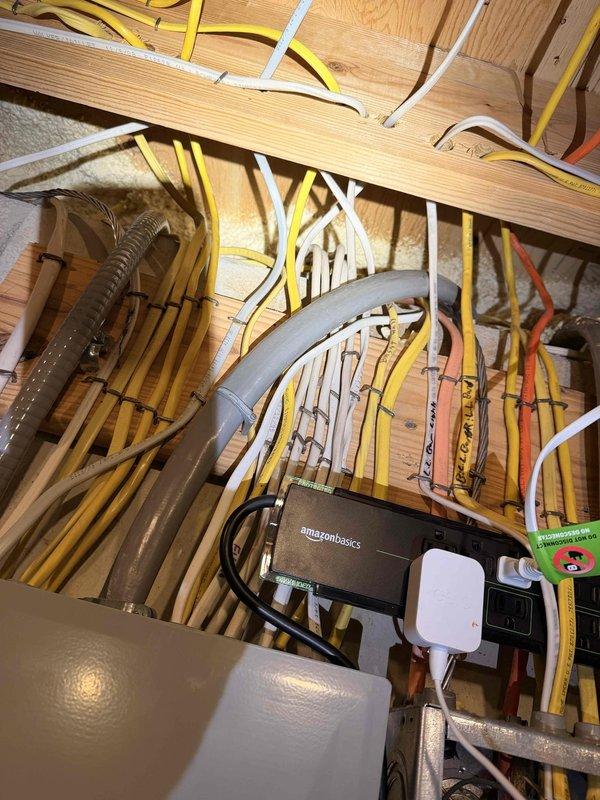 Conducted site assessment for installation of new electrical conductor from second-floor distribution panel to exterior AC disconnect switch. Inspection revealed complex cable routing through structural framework with multiple existing electrical and communication lines. Examined exterior connection point where service entrance will terminate, noting weathered junction box mounted on vinyl siding that will require proper sealing during installation to prevent moisture intrusion.